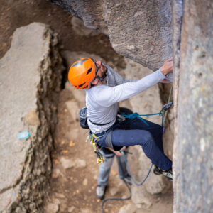 Expert climbing guide leading a traditional route, demonstrating gear placement for trad climbing students.